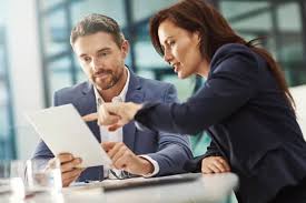 Man and woman in business attire sitting at a table, looking at a document.