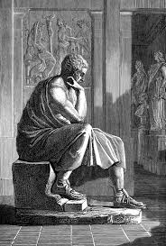 A statue of a man sitting on a stone bench, wearing a toga and sandals, with his hand to his chin, in a dimly lit room wit...